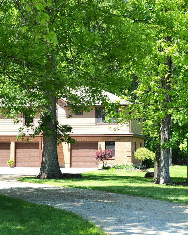 Long driveway curving through a green lawn and mature trees to a two-storey home with three garage doors