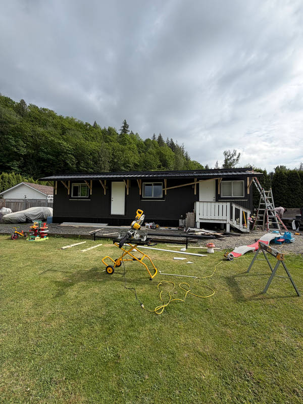 Black-sided single-storey home mid-renovation, with a mitre saw and sawhorses set up on the lawn
